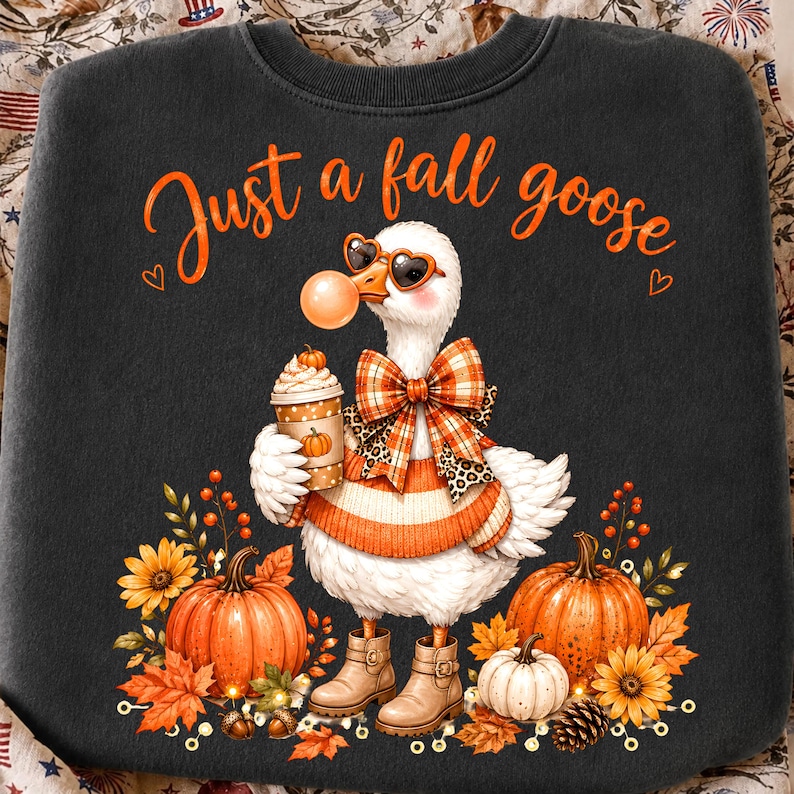 May include: A dark grey sweatshirt featuring a white goose wearing heart-shaped sunglasses, a plaid bow, and an orange sweater. The goose holds a coffee cup with a pumpkin design. The text reads Just a fall goose, surrounded by pumpkins and leaves.
