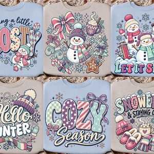 May include: Six crewneck sweatshirts featuring winter-themed graphic prints. Designs include snowmen, snowflakes, mugs of cocoa, mittens, and scarves with text such as feeling a little FROSTY, LET IT SNOW, Hello WINTER, COZY Season, and SNOWED IN & STAYING COZY.