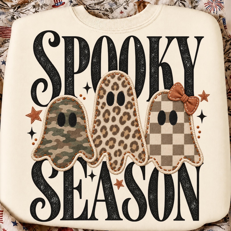 K&ouml;nnte beinhalten: Ein cremefarbenes Sweatshirt mit dem schwarzen Schriftzug SPOOKY SEASON und drei Geisterfiguren. Die Geister haben verschiedene Muster: eines in Camouflage, eines mit Leopardenmuster und eines kariert mit einer kleinen braunen Schleife.