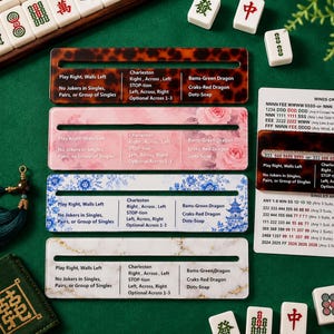 May include: Four rectangular Mahjong tile racks featuring distinct patterns: tortoise shell, pink roses, blue floral with a pagoda, and white marble with gold veining. Each rack includes a horizontal slot and printed Mahjong strategy text.