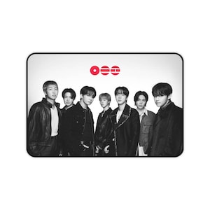 May include: A rectangular desk mat featuring a black and white photograph of seven individuals standing in a row. Above the group, there is a red logo consisting of three circular and horizontal line icons. The mat has a black border.
