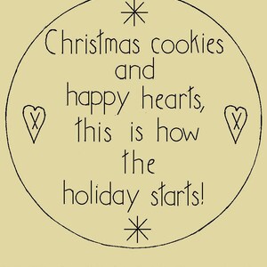 May include: A round, cream-colored candle mat with the text "Christmas cookies and happy hearts, this is how the holiday starts!" in black script. The mat measures 7.5 x 7.5 inches and features star and heart accents.