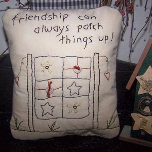 May include: Cream-colored pillow with embroidered design and text reading "friendship can always patch things up!". The pillow features a fence design with flowers, stars, and buttons. A decorative green and brown birdhouse is next to the pillow.