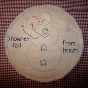 May include: A white fabric circle with a hand-stitched snowman design. The snowman has a carrot nose, black eyes, and blue star buttons. The text "Snowmen fall from heaven." is stitched around the snowman.