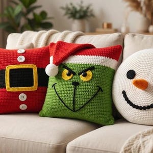 May include: Three crochet pillows featuring holiday designs: a red square pillow with a black belt and white buttons, a green square pillow with a red hat and a grumpy face, and a round white snowman pillow with a black hat and orange nose.