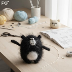 May include: A fuzzy black and white needle-felted cat figurine with a round body, small ears, and a white belly patch. The cat has a white muzzle, black eyes, and thin whiskers. A PDF label is visible in the top left corner of the image.