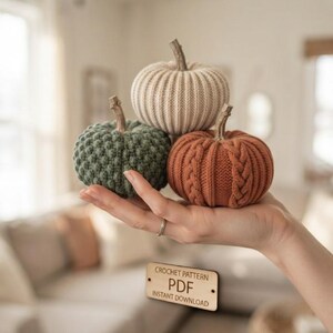 May include: Three small crocheted pumpkins in cream, sage green, and burnt orange, each featuring a textured knit pattern and a brown stem. A rectangular wooden sign below displays the text CROCHET PATTERN PDF INSTANT DOWNLOAD.