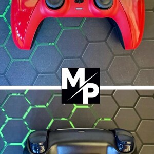Op de afbeelding: Een draadloze videogamecontroller met een glanzende rood-zwarte gradiëntafwerking aan de voorzijde, zwarte analoge sticks, knoppen en een centraal touchpad. De achterkant is matzwart met getextureerde grepen en een bevestigd achterknopaccessoire.
