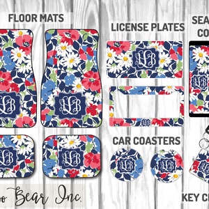 Puede incluir: Conjunto de accesorios para coche con diseño floral, que incluye alfombrillas, matrículas, fundas para cinturones de seguridad, posavasos y un llavero. El diseño presenta flores rojas, azules y blancas sobre un fondo azul marino, con un monograma. El texto es visible.