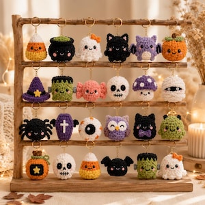May include: A wooden display rack holding twenty-four crocheted Halloween-themed keychains. The collection includes miniature figures of ghosts, pumpkins, skulls, spiders, bats, candy corn, mummies, monsters, owls, and mushrooms in various colors.