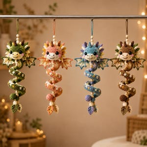 May include: Four hanging crochet dragon ornaments in green, peach, blue, and brown. Each dragon features a coiled body decorated with small white flowers, a pair of wings, a round head with black eyes, and a hanging loop with wooden beads.