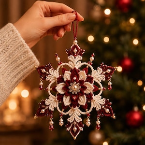 May include: A decorative snowflake ornament crafted from intricate crochet in deep red and cream yarn. The design features layered floral petals, small white pearl beads, and dangling red crystal teardrops, suspended by a thin red cord loop.