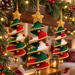 Op de afbeelding: Drie spiraalvormige kerstboomhangers van gehaakt garen met afwisselende banen in donkergroen, rood en wit. Elke hanger is bekroond met een gouden gehaakte ster en versierd met gouden koord, kleine rode en gouden kralen en een gouden belletje.