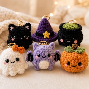 May include: A collection of six crocheted keychains featuring a black cat, a purple witch hat with a yellow star, a black cauldron with green contents, a white ghost with an orange bow, a purple bat, and an orange pumpkin with green leaves.