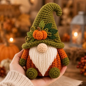 Op de afbeelding: Een gehaakt kabouterfiguurtje met een olijfgroene puntmuts versierd met een kleine oranje pompoen en donkergroene bladeren. De kabouter heeft een ronde beige neus, een lange witte garen baard, een oranje lichaam en olijfgroene handen en voeten.