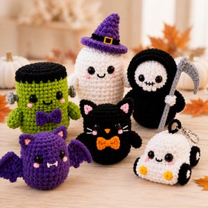 May include: A collection of six crocheted Halloween figures including a green monster with a purple bow, a white ghost in a purple hat, a black grim reaper with a scythe, a purple bat, a black cat with an orange bow, and a white ghost car keychain.