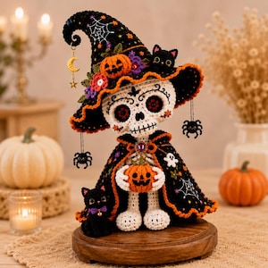 May include: A crocheted skeleton figurine wearing a black witch hat with orange trim, spiderweb embroidery, and a small black cat. The skeleton wears a black cape with orange trim and holds a small orange pumpkin, with a black cat sitting nearby.