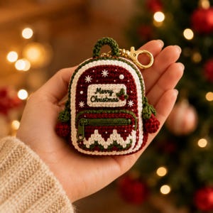 Può includere: Un portachiavi a forma di zainetto in miniatura realizzato all'uncinetto con filati rosso scuro, verde bosco e crema. Il davanti presenta una toppa color crema con la scritta Merry Christmas, una tasca con zip verde e bacche rosse. Gancio dorato.