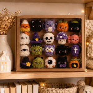 May include: A cardboard display box containing sixteen small, crocheted Halloween-themed figures. The collection includes a candy corn, black cat, bat, pumpkin, cauldron, ghost, witch hat, skull, mushroom, candy, mummy, Frankenstein, owl, spider, coffin, and eyeball.