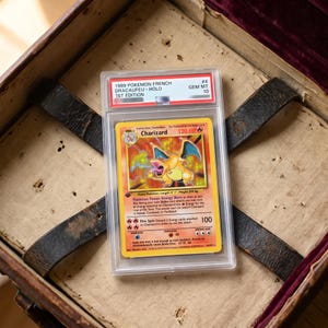 Könnte beinhalten: Eine bewertete 1989 French 1st Edition Charizard holografische Pokemon-Sammelkarte in einer durchsichtigen Kunststoff-Schutzhülle. Das Etikett lautet 1989 POKEMON FRENCH DRACAUFEU - HOLO 1ST EDITION GEM MT 10. Die Karte zeigt einen feuerspeienden Drachen.