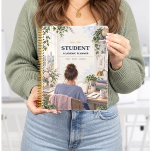 Könnte beinhalten: Ein spiralgebundener 2026-2027 Studentenplaner mit einer Titelillustration, die eine Person an einem Schreibtisch mit Büchern, Pflanzen und einer Lampe zeigt. Der Text lautet STUDENT ACADEMIC PLANNER und PLAN STUDY ACHIEVE in dunkelblau.