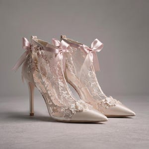 May include: A pair of pale pink high-heeled pumps featuring sheer lace overlays with intricate floral embroidery, small pearl accents, and a satin ribbon bow tied at the ankle. The shoes have a pointed toe and a slim stiletto heel design.