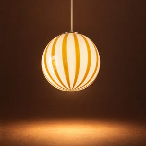 Op de afbeelding: Een bolvormige hanglamp met een witte glazen bol voorzien van verticale gele strepen. De bol hangt aan een dunne, rechte metalen stang die vanuit het midden van de bovenkant van de bol omhoog loopt, wat zorgt voor een strak en symmetrisch ontwerp.