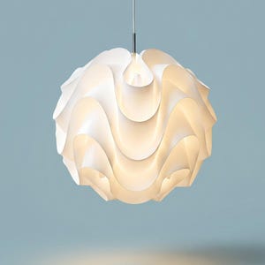 May include: A spherical pendant light fitting featuring a series of overlapping, curved white panels that create a wavy, layered texture. The lamp is suspended by a thin, straight metal rod and emits a soft, warm glow from its centre.