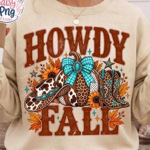 May include: A beige crewneck sweatshirt featuring a graphic print with the text HOWDY FALL in brown letters. The design includes a pumpkin with a turquoise bow, a cow print cowboy hat, leopard print cowboy boots, sunflowers, and autumn leaves.