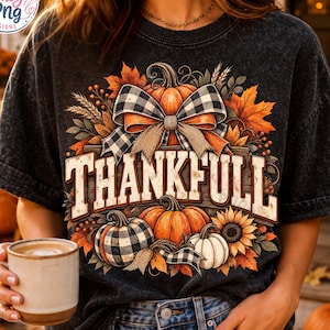 May include: A charcoal grey mineral-wash t-shirt featuring a graphic print of pumpkins, sunflowers, autumn leaves, and a black and white buffalo plaid bow. The text THANKFULL is printed in large, bold, off-white letters across the center of the design.