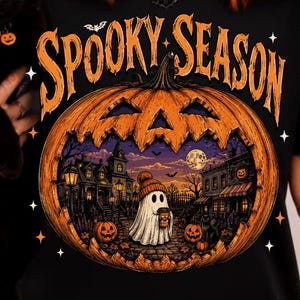 May include: A black t-shirt featuring a large orange pumpkin graphic with the text "SPOOKY SEASON" in orange letters. The pumpkin contains a detailed scene of a ghost wearing a beanie, a haunted house, and a full moon under a starry night sky.