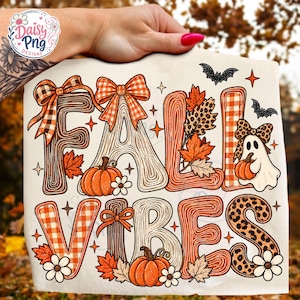 Könnte beinhalten: Eine weiße Stoffoberfläche mit dem Schriftzug FALL VIBES in großen, stilisierten Buchstaben, verziert mit orangefarbenen Karomustern, Holzmaserung und Leopardenmuster, akzentuiert durch Kürbisse, Herbstblätter, Gänseblümchen, Fledermäuse und ein kleines Gespenst mit einer Schleife.