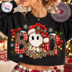 Könnte beinhalten: Ein schwarzes Langarm-Sweatshirt mit einer Grafik eines Geistes mit Weihnachtsmütze, umgeben vom Schriftzug BOO. Die Buchstaben sind mit Leopardenmuster und rotem Schottenkaro verziert, akzentuiert durch Lichterketten, Schleifen und Stechpalmen.