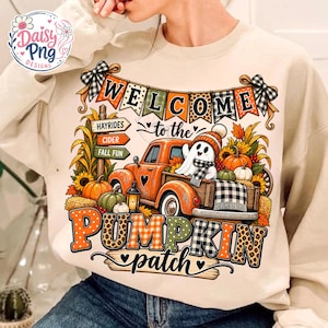 Könnte beinhalten: Ein beigefarbenes Sweatshirt mit Rundhalsausschnitt und einem Grafikdruck eines orangefarbenen Lastwagens, eines Geistes, Kürbissen und Sonnenblumen. Der Text lautet "WELCOME to the PUMPKIN patch" mit "HAYRIDES", "CIDER" und "FALL FUN" auf Schildern.