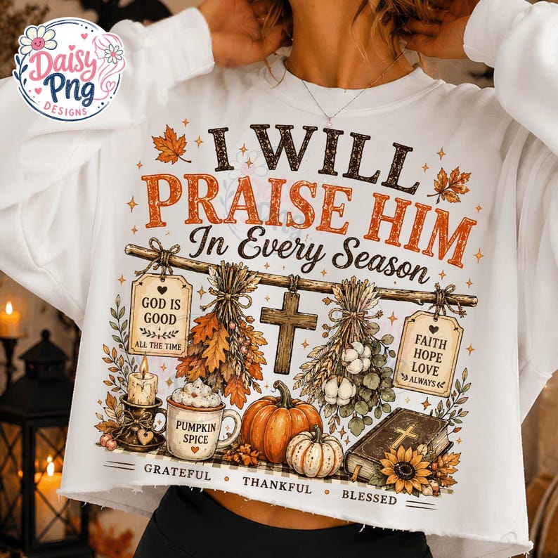 May include: A white long-sleeve sweatshirt featuring a graphic print with the text I WILL PRAISE HIM In Every Season, God Is Good, Faith Hope Love, Pumpkin Spice, Grateful, Thankful, Blessed, a cross, pumpkins, a candle, and a book.