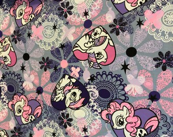 May include: A colorful fabric with a repeating pattern of cartoon ponies in hearts, flowers, and swirls. The background is a light gray with pink, purple, and white accents.