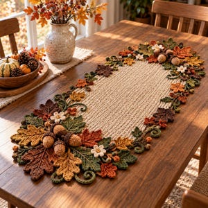 May include: An oval crochet table runner featuring a central beige textured weave bordered by intricate, three-dimensional autumn-themed embellishments including crocheted oak leaves in brown, orange, and green, small white flowers, and acorns.
