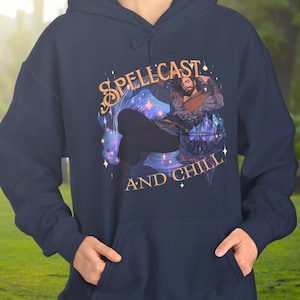 Puede incluir: Una sudadera con capucha azul marino con un gráfico de una persona en una pose mágica con el texto "SPELLCAST AND CHILL" en letras doradas.