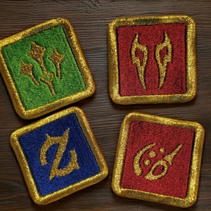 May include: Four square embroidered patches with gold trim. Each patch features a different symbol in gold on a colored background: green, red, blue, and red. The patches are displayed on a dark wood surface.