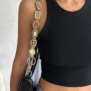 Puede incluir: Un bolso de hombro negro con una correa única construida a partir de una serie de relojes de pulsera dorados de estilo vintage en varias formas, incluyendo esferas rectangulares, de corazón y redondas con diversos colores de fondo.