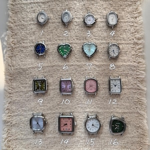 May include: A collection of sixteen silver-tone watch faces in various shapes including round, oval, heart, square, and rectangular. Each watch face features a unique dial color such as blue, green, pink, and white, labeled with numbers 1 through 16.