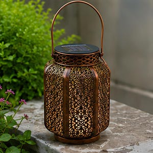 May include: A copper-colored metal lantern with an intricate laser-cut filigree pattern and a top handle. The lantern features a circular solar panel on the lid and emits a warm internal glow through the detailed cutouts in the cylindrical body.