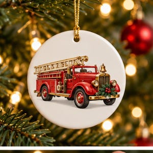 May include: A round white ceramic ornament featuring a detailed illustration of a vintage red fire truck with a gold ladder on top, a gold bell, and a small green wreath with red berries attached to the front grille, suspended by a gold cord.