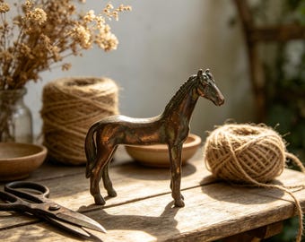 Puede incluir: Una figura de caballo en tono bronce con un acabado metálico liso. La escultura representa un caballo en una pose neutral con crines y cola definidas, mostrando una pátina oscura y desgastada en toda su superficie.