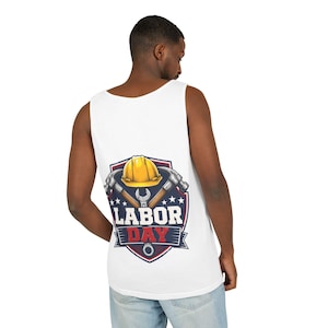 May include: A white tank top featuring a graphic on the back with a yellow hard hat, two crossed hammers, and a wrench inside a blue shield emblem. The text "LABOR DAY" is printed in bold white and red letters across the center of the shield design.