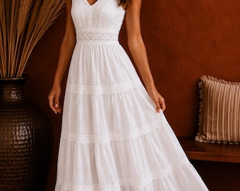 May include: A floor-length white sleeveless dress featuring a V-neckline, a fitted bodice with lace detailing at the waist, and a tiered skirt with horizontal lace trim inserts. The fabric has a subtle textured pattern and a scalloped lace hem.