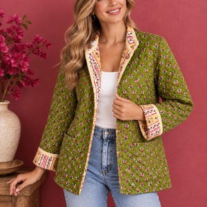 May include: A quilted olive green jacket featuring a repeating floral pattern in pink and white. The jacket has long sleeves with folded cuffs, a straight hem, and two front pockets. The inner lining and trim display a contrasting striped floral print.
