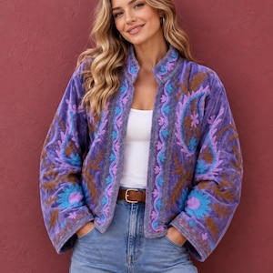May include: A purple velvet jacket featuring long sleeves and an open front. The garment is decorated with intricate embroidery in shades of light blue, lavender, and brown, showcasing floral and paisley patterns along the collar and front edges.