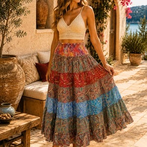 Puede incluir: Un top corto de ganchillo color crema con tirantes finos y escote en V, combinado con una falda larga de capas con un estampado de cachemira multicolor en tonos rojos, azules y marrones con una cintura elástica fruncida.