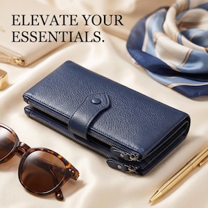 May include: A navy blue textured wallet with a snap button closure and two side zippers. The wallet features the text ELEVATE YOUR ESSENTIALS. It is accompanied by tortoise shell sunglasses, a gold pen, and a blue and white patterned scarf.